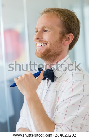 Happy businessman looking away while holding felt tip pen at creative office