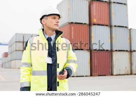 Middle-aged man holding walkie-talkie in shipping yard