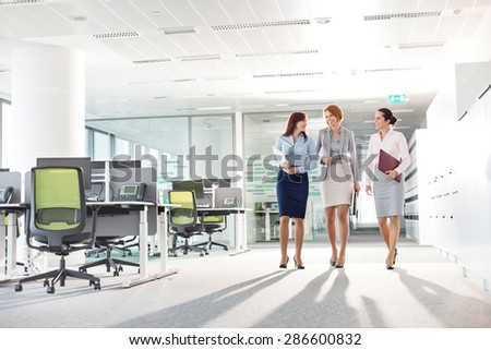 Full-length of businesswomen with file folders walking in office