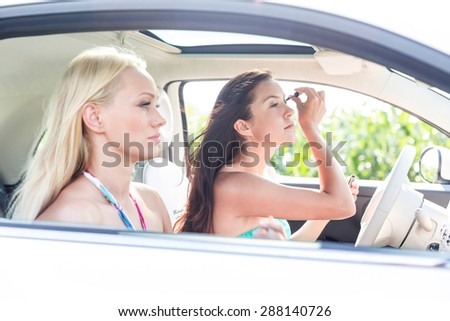 Woman doing make-up with female friend sitting in car