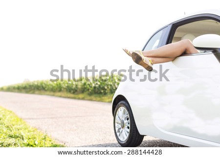 Low section of woman relaxing in car on country road
