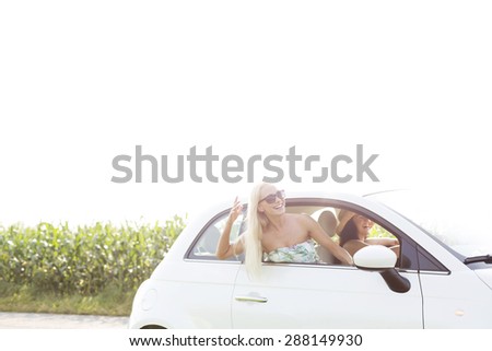Happy female friends enjoying in car against clear sky