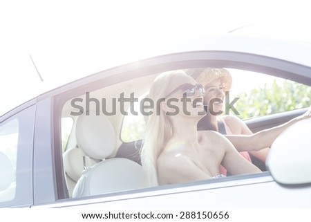 Happy female friends enjoying road trip in car on sunny day