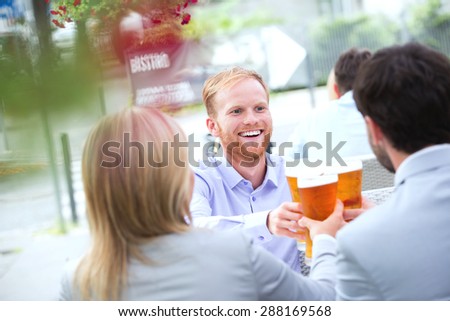 Happy businessman toasting beer glass with colleagues at outdoor restaurant