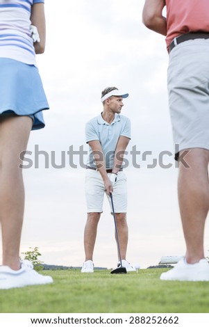 Man playing golf against sky with friends standing in foreground