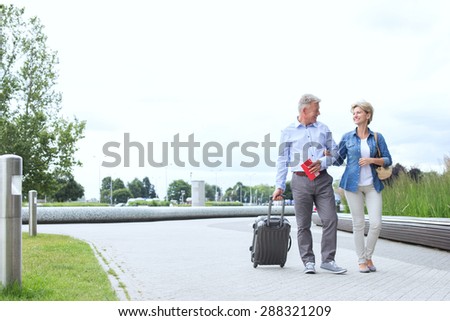 Middle-aged couple with luggage walking on footpath against clear sky