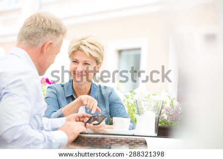 Happy middle-aged couple using cell phone at sidewalk cafe