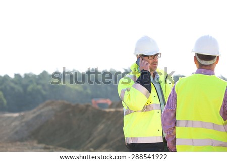 Supervisor using mobile phone while standing with colleague at construction site against clear sky