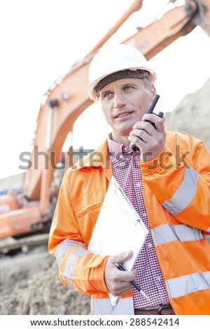 Supervisor holding clipboard while using walkie-talkie at construction site