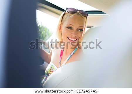 Happy beautiful woman looking back while driving car