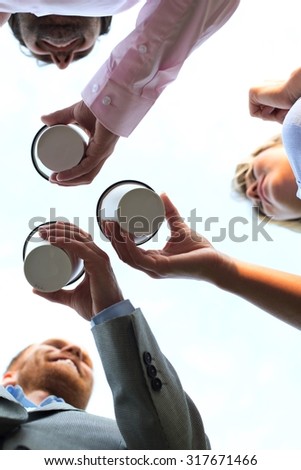 Directly below shot of businesspeople holding disposable cups against clear sky