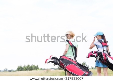 Rear view of women with golf club bags at course against clear sky
