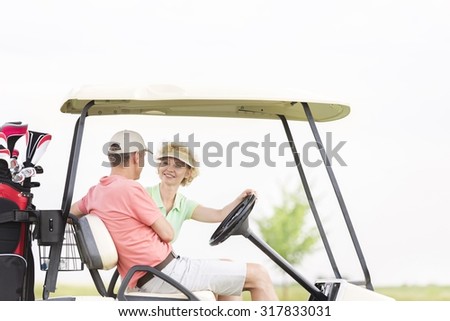 Happy woman looking at man while sitting in golf cart