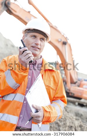 Supervisor holding clipboard while using walkie-talkie at construction site