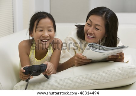 Mother and Daughter Playing Video Game and Reading on Couch
