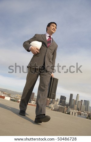 Business man carrying hard hat on city rooftop