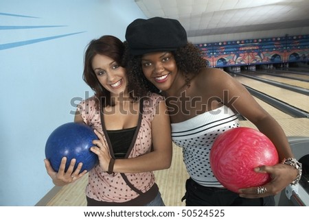 Young women at bowling alley holding balls, portrait
