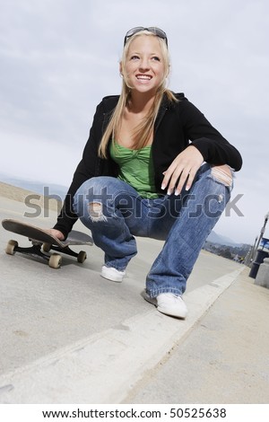 Young female skateboarder crouching on pavement, low angle view