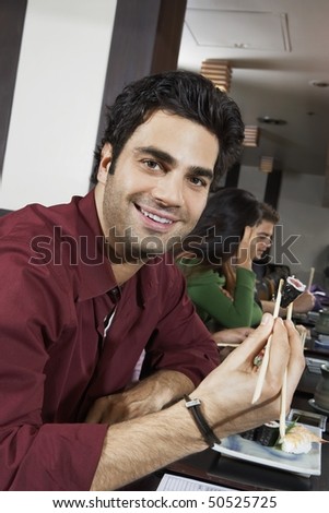 Young people eating sushi with chopsticks in restaurant