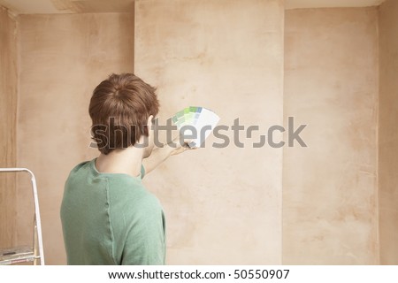 Man looking at paint colour swatches in unrenovated room, back view