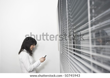 Female office worker using mobile phone in front of office window, side view