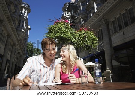 Young couple sitting at outdoor cafe writing postcard