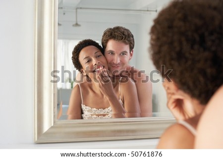 Man embracing woman applying lipstick in mirror