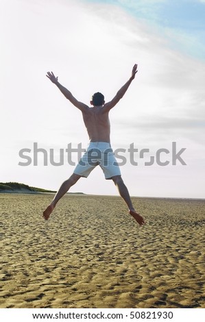 Man on beach doing star jump, back view