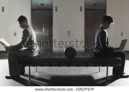 Businessmen sitting on bench  in Lobby, working on laptops, reading newspaper, side view