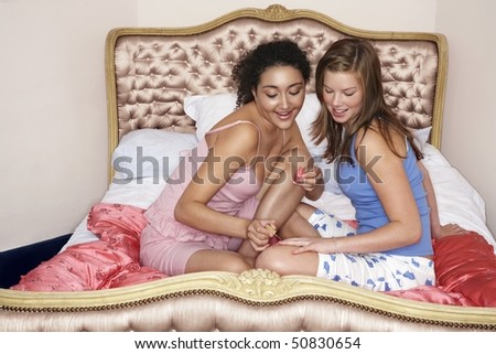 Teenage girl painting friend\'s fingernails on bed at slumber party