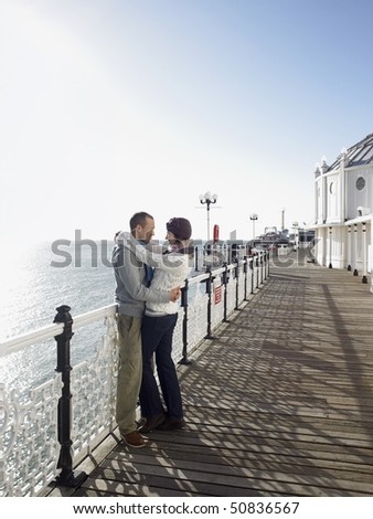 Couple embracing, standing on pier, side view, full length
