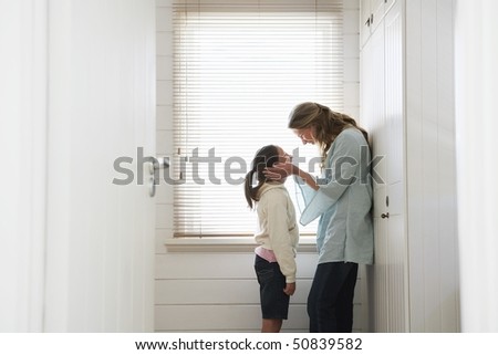 Mother cupping daughters face in hands, standing by window