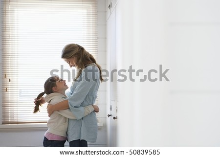Mother and daughter embracing standing in front of window