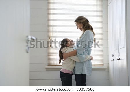 Mother and daughter hugging, standing in front of  window