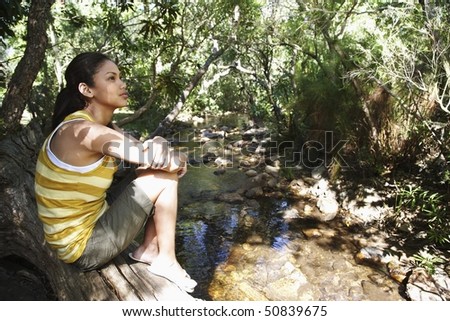Teenage girl (16-17 years) sitting on tree trunk by stream in forest
