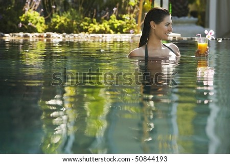 Young woman holding drink in natural swimming pool, portrait
