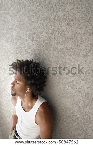 Young man leaning against wall listening to music through headphones, portrait