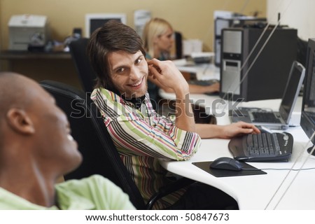 Three people sitting at desk using computers, two men talking.