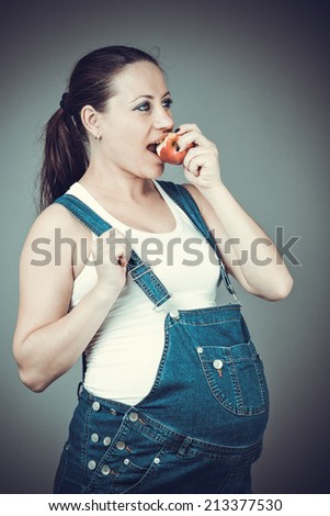 Pregnant beautiful girl in denim overalls. Pregnant woman posing on a gray background