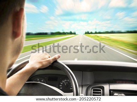 Man\'s hands of a driver on steering wheel of a minivan car on asphalt road