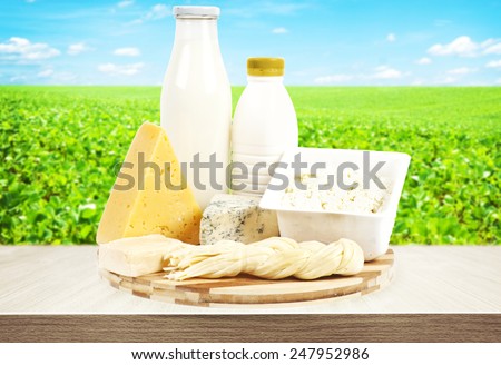 Dairy products on wooden table and field with green grass on background