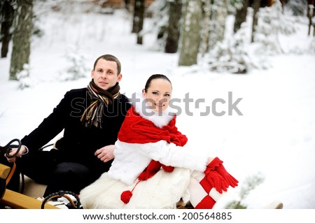 Young elegant couple sitting on sledge. Winter forest background.