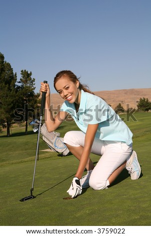 A pretty woman golfer retrieving her ball from the hole