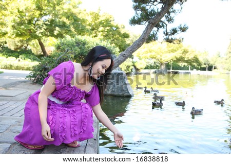 A pretty asian woman playing with fish in pond