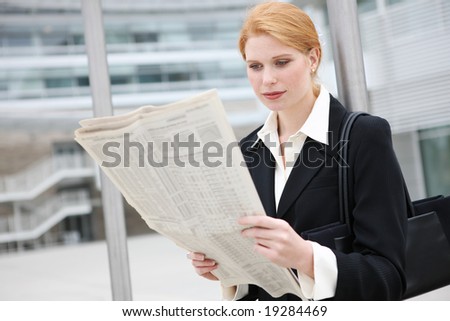 A pretty, young business woman at office building reading newspaper