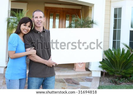 An attractive happy couple in front of their home holding a sign