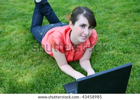 A cute young woman student on computer on grass in the park