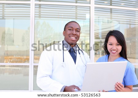 An ethnic medical man and woman team outside hospital on laptop computer