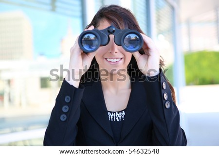 Young caucasian business woman looking through binoculars at office building
