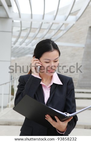 A pretty Chinese business woman smiling outside office building on phone